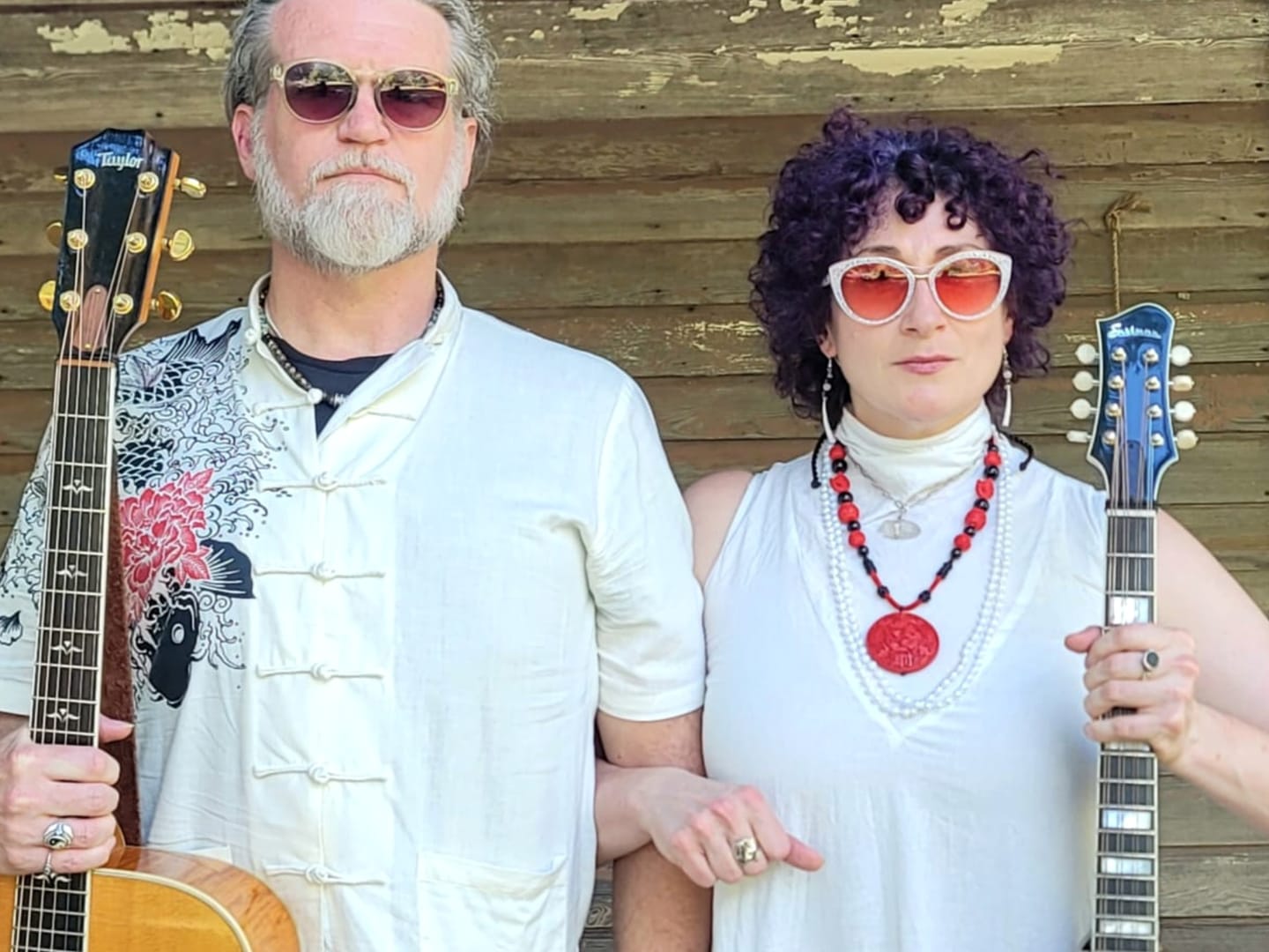 Kristi and Steven outside a clapboard house holding their guitars upright like pitchforks