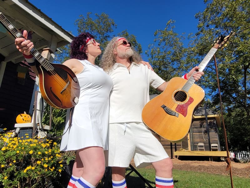 The duo in white, shot from below against a blue sky, guitars raised