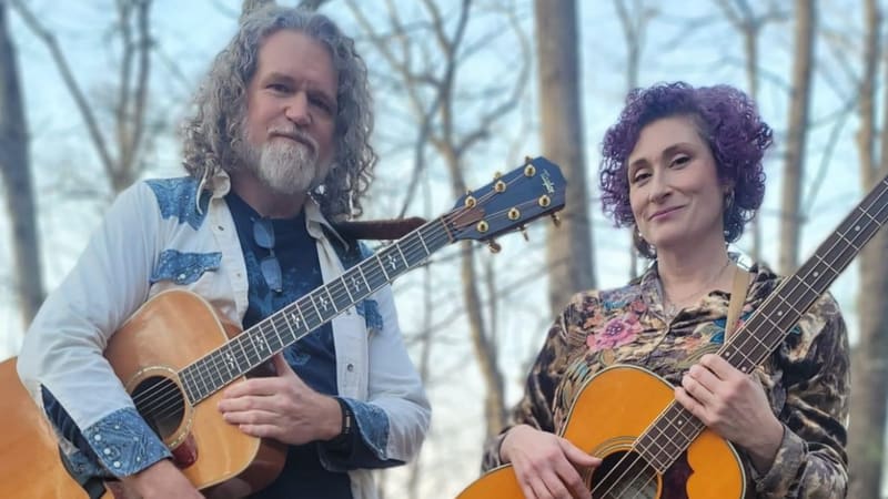 Steven and Kristi outdoors with acoustic guitars among bare trees